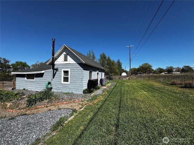 view of side of home with roof with shingles, fence, and a lawn