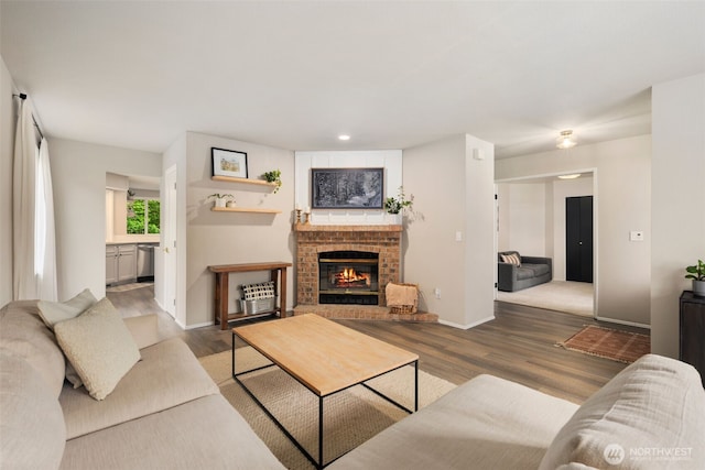 living area with wood finished floors, baseboards, a brick fireplace, and recessed lighting