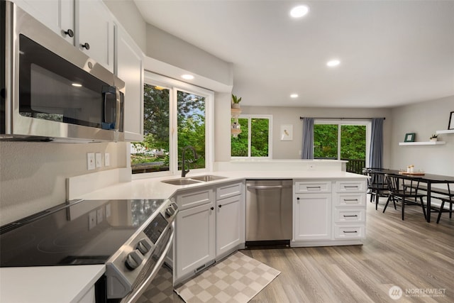 kitchen with stainless steel appliances, a sink, white cabinets, recessed lighting, and light wood-type flooring