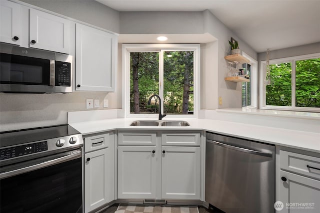 kitchen featuring stainless steel appliances, a sink, light countertops, and open shelves