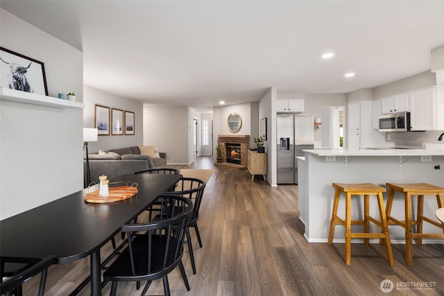 kitchen featuring stainless steel appliances, a fireplace, a peninsula, white cabinetry, and a kitchen breakfast bar