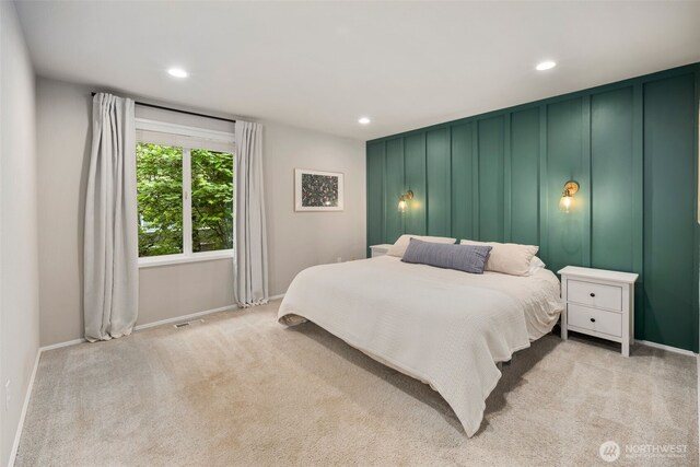 bedroom with baseboards, light carpet, recessed lighting, and a decorative wall