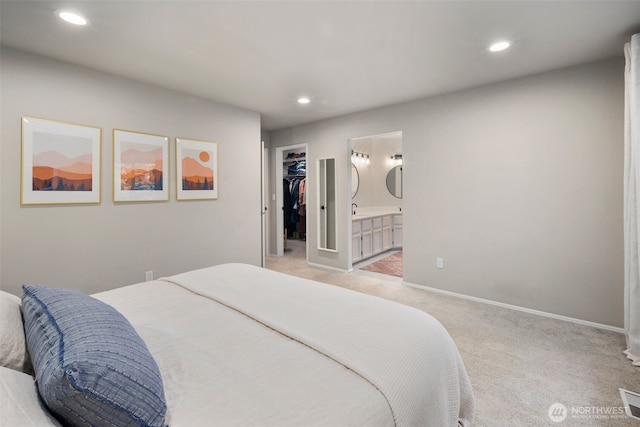 bedroom with light colored carpet, recessed lighting, a walk in closet, ensuite bath, and baseboards