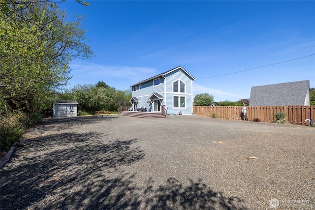 back of house with fence, a storage shed, an outdoor structure, and driveway