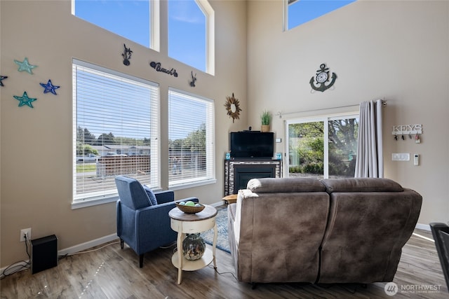 living room featuring a towering ceiling, baseboards, wood finished floors, and a glass covered fireplace