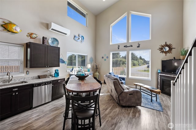 kitchen with dishwasher, a sink, a wall mounted AC, a towering ceiling, and light wood-style flooring