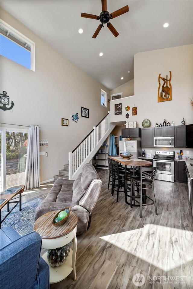 living area featuring stairway, high vaulted ceiling, ceiling fan, light wood-style floors, and recessed lighting
