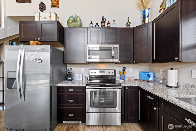 kitchen with stainless steel appliances, dark brown cabinets, light stone countertops, and light wood-style flooring
