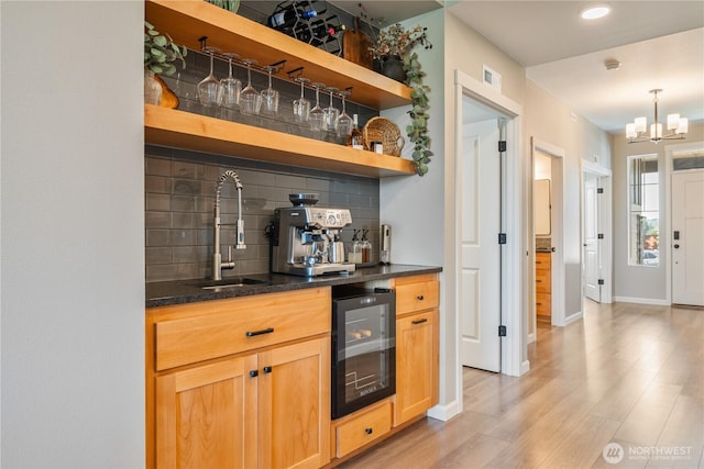 indoor wet bar featuring wine cooler, decorative backsplash, light wood-style flooring, a chandelier, and baseboards