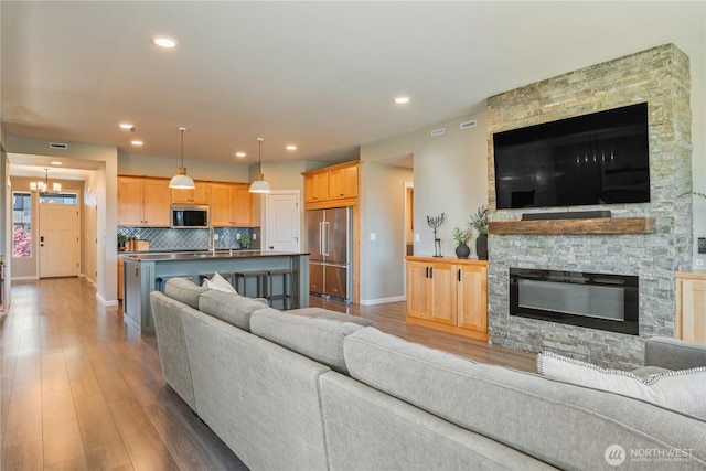 living area featuring baseboards, light wood-style floors, a fireplace, a chandelier, and recessed lighting