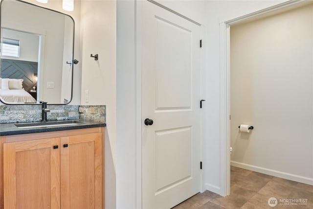 bathroom featuring vanity, tasteful backsplash, baseboards, and ensuite bathroom