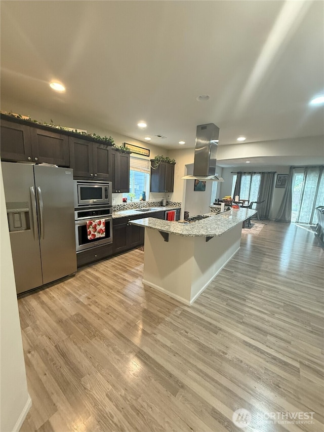 17510 80th Avenue Ct E, Puyallup, WA 98375 - kitchen with a breakfast bar area, stainless steel appliances, range hood, light wood-type flooring, and light stone countertops