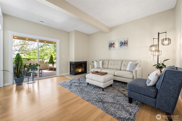 living area featuring wood finished floors, a multi sided fireplace, beam ceiling, and baseboards
