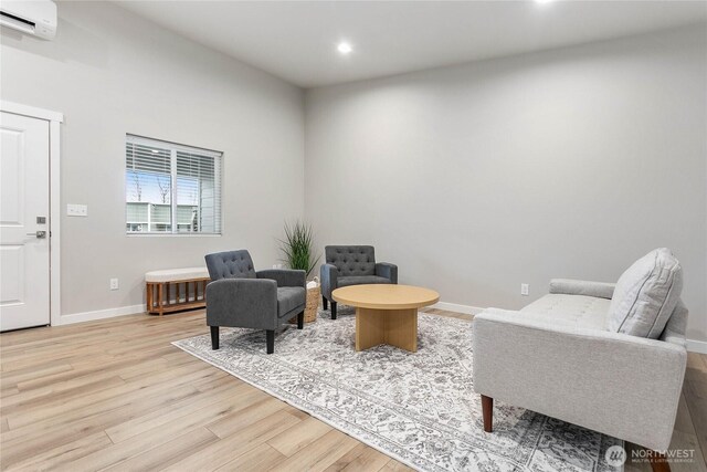 living area with an AC wall unit, light wood finished floors, baseboards, and recessed lighting