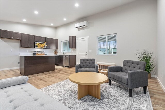 living area with a wall mounted air conditioner, light wood-type flooring, recessed lighting, a towering ceiling, and baseboards
