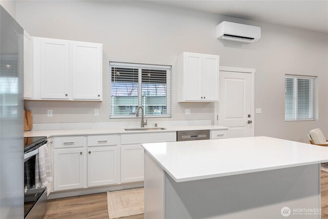 kitchen with a sink, a wall unit AC, appliances with stainless steel finishes, light wood finished floors, and light countertops