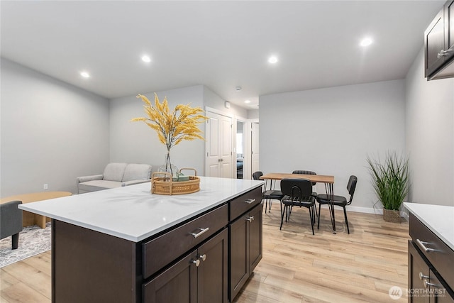 kitchen featuring light countertops, light wood-type flooring, dark brown cabinets, recessed lighting, and a kitchen island