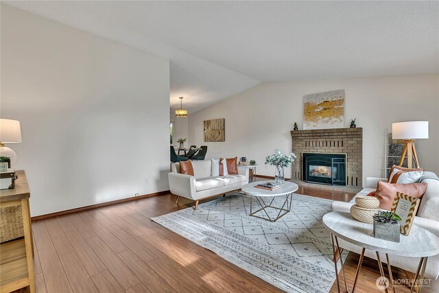 living room with vaulted ceiling, wood finished floors, a brick fireplace, and baseboards