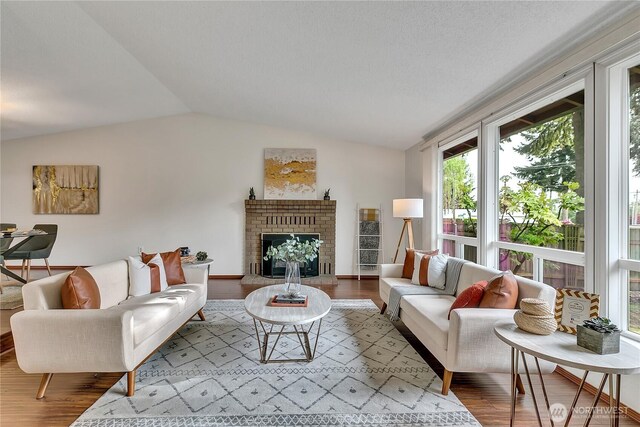 living room with wood finished floors, vaulted ceiling, and a brick fireplace
