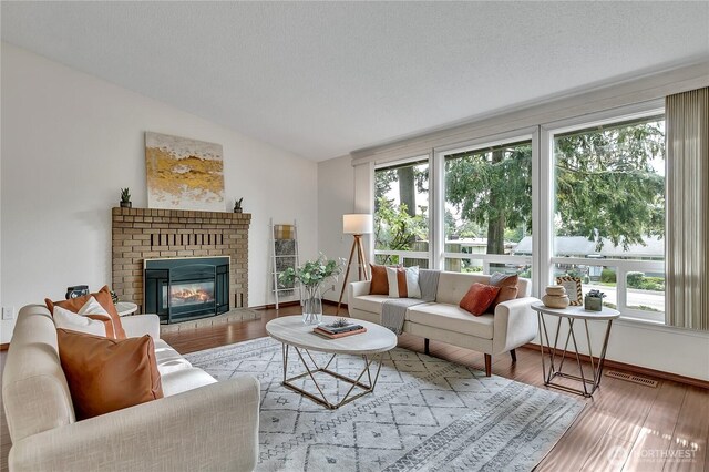 living area with wood finished floors, vaulted ceiling, a brick fireplace, and baseboards