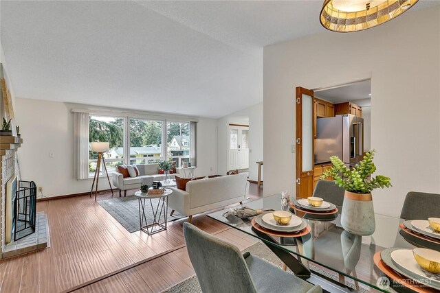 dining area with a fireplace, vaulted ceiling, light wood-style floors, and baseboards
