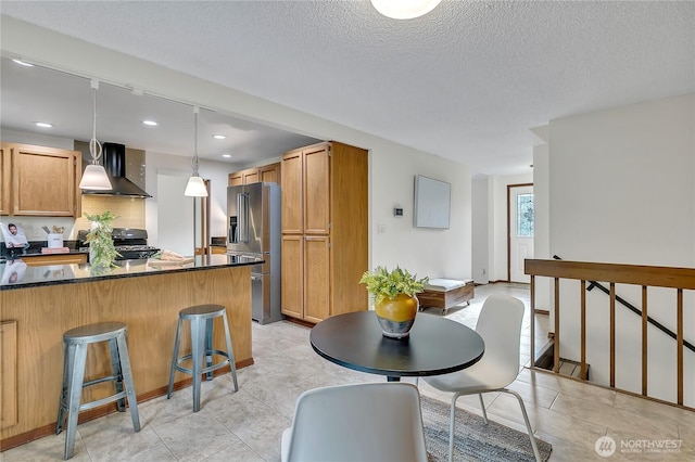 kitchen featuring high end fridge, wall chimney range hood, a kitchen bar, a textured ceiling, and recessed lighting