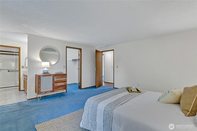 bedroom with light colored carpet, a spacious closet, ensuite bathroom, a closet, and a textured ceiling