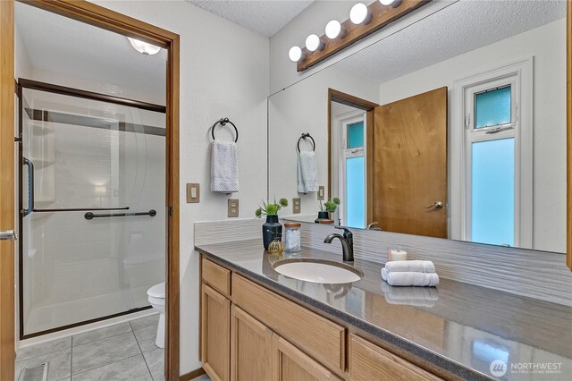 bathroom featuring a stall shower, toilet, vanity, a textured ceiling, and tile patterned flooring