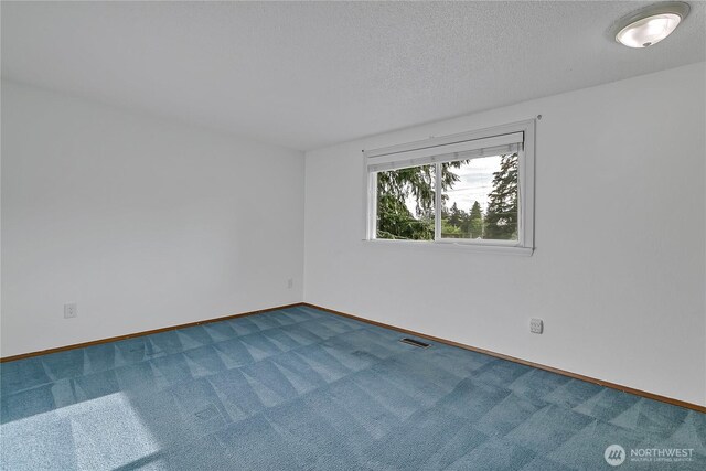 spare room featuring dark carpet, baseboards, and a textured ceiling