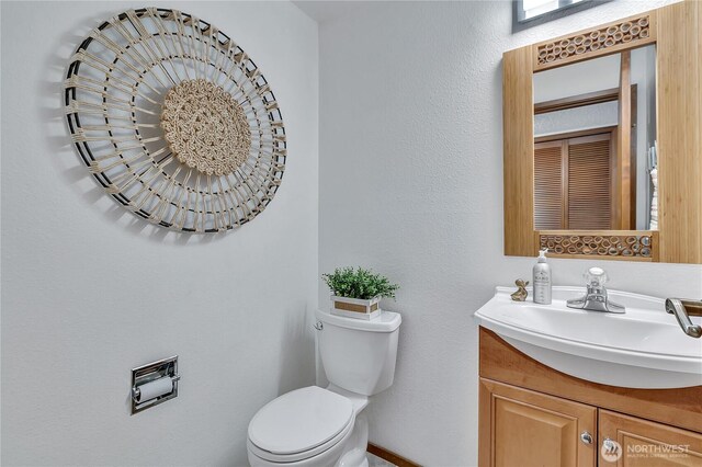 bathroom with toilet, vanity, and a textured wall