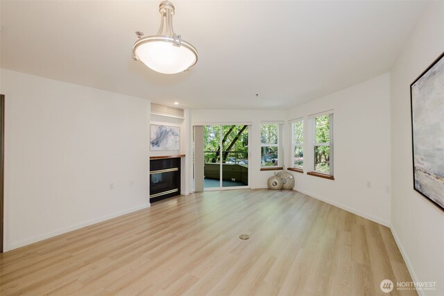1750 152nd Ave NE Unit W110, Bellevue, WA 98007 - unfurnished living room with light wood finished floors, a glass covered fireplace, and baseboards