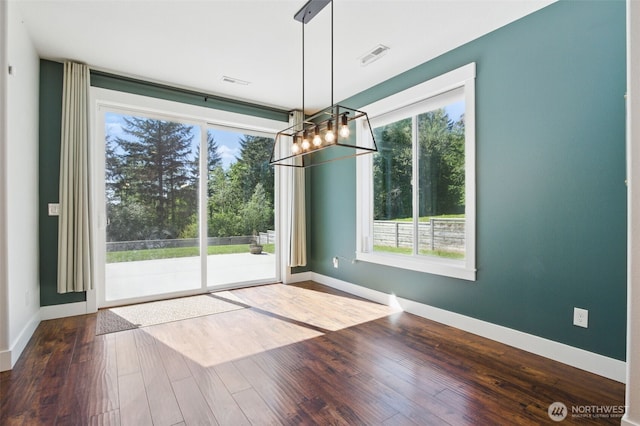 unfurnished dining area featuring a chandelier, healthy amount of natural light, and wood finished floors