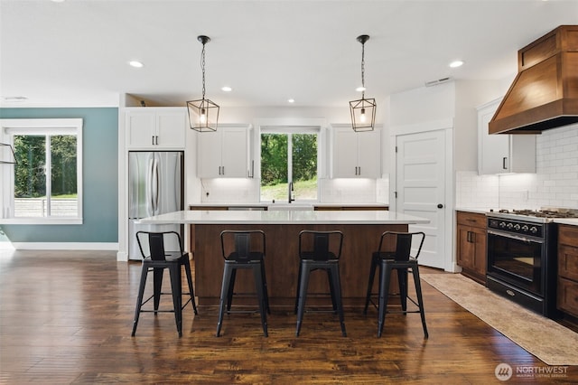 kitchen with freestanding refrigerator, gas stove, premium range hood, a kitchen island, and backsplash