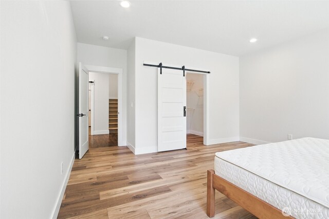 bedroom featuring a barn door, light wood finished floors, baseboards, recessed lighting, and a walk in closet