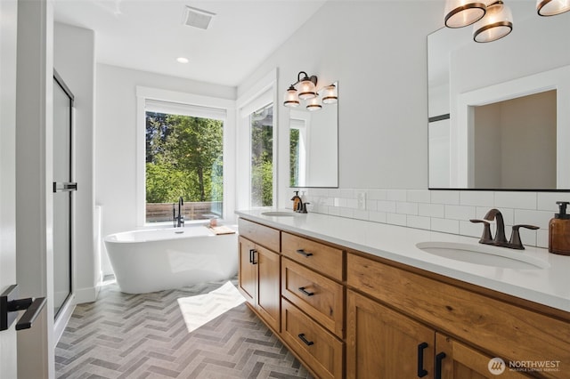 bathroom featuring backsplash, a freestanding tub, double vanity, recessed lighting, and an enclosed shower
