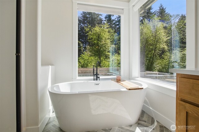 bathroom featuring a freestanding bath, plenty of natural light, and baseboards