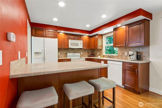 kitchen with white appliances, a peninsula, light wood-style floors, light countertops, and decorative backsplash