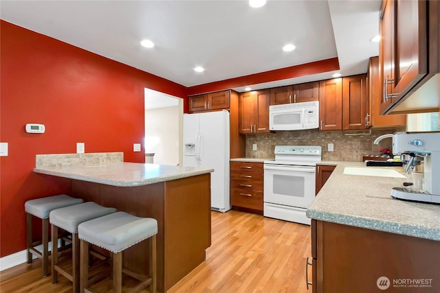 kitchen featuring white appliances, a breakfast bar, a peninsula, tasteful backsplash, and light wood-style flooring