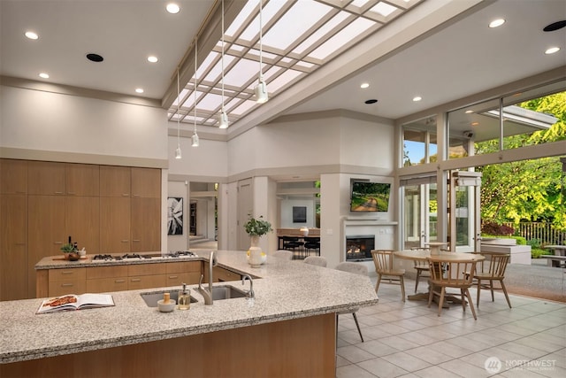 kitchen with a towering ceiling, a glass covered fireplace, light tile patterned floors, a sink, and gas cooktop