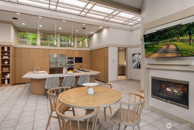 dining area featuring light tile patterned floors, a glass covered fireplace, a high ceiling, and recessed lighting