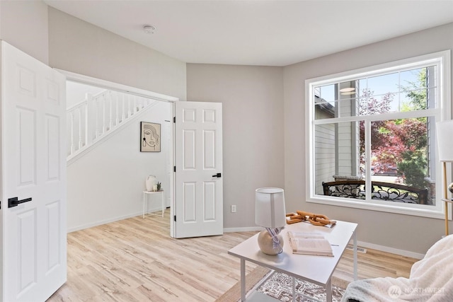 living area featuring stairs, light wood finished floors, and baseboards