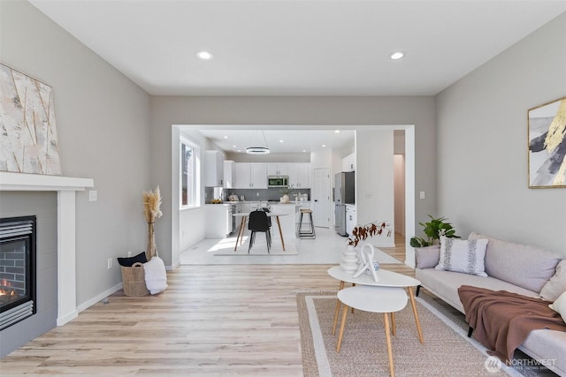 living room featuring light wood-style flooring, a tile fireplace, and recessed lighting