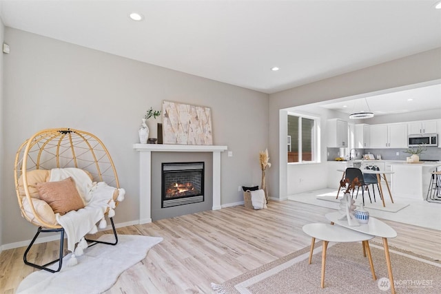 living area featuring light wood finished floors, recessed lighting, a glass covered fireplace, and baseboards