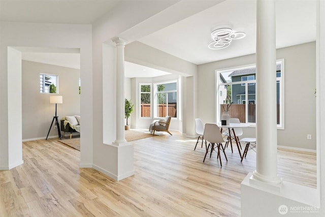 dining space featuring decorative columns, light wood finished floors, and baseboards