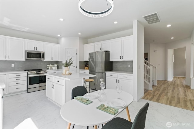 kitchen featuring appliances with stainless steel finishes, backsplash, a kitchen island, recessed lighting, and light countertops