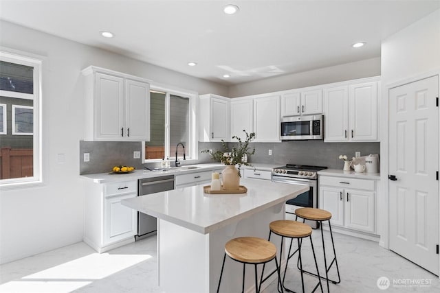 kitchen with stainless steel appliances, light marble finish flooring, a breakfast bar area, recessed lighting, and white cabinets