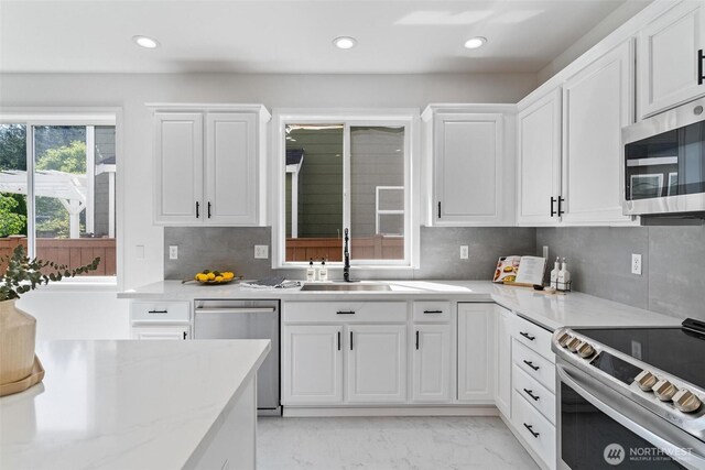 kitchen with a sink, appliances with stainless steel finishes, white cabinetry, backsplash, and recessed lighting