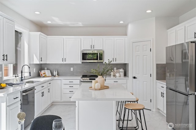 kitchen featuring stainless steel appliances, light marble finish flooring, a sink, a kitchen island, and recessed lighting