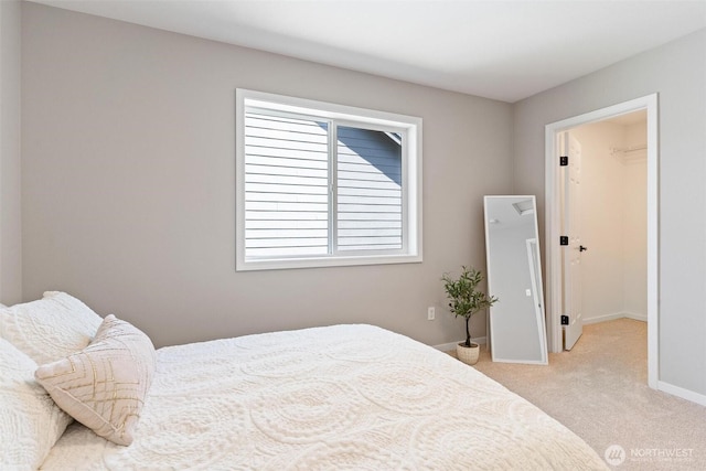bedroom featuring light colored carpet, a walk in closet, and baseboards