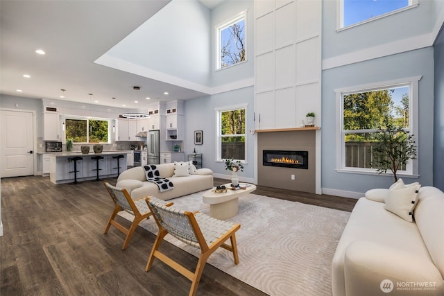 living area with a towering ceiling, dark wood-style floors, recessed lighting, baseboards, and a glass covered fireplace